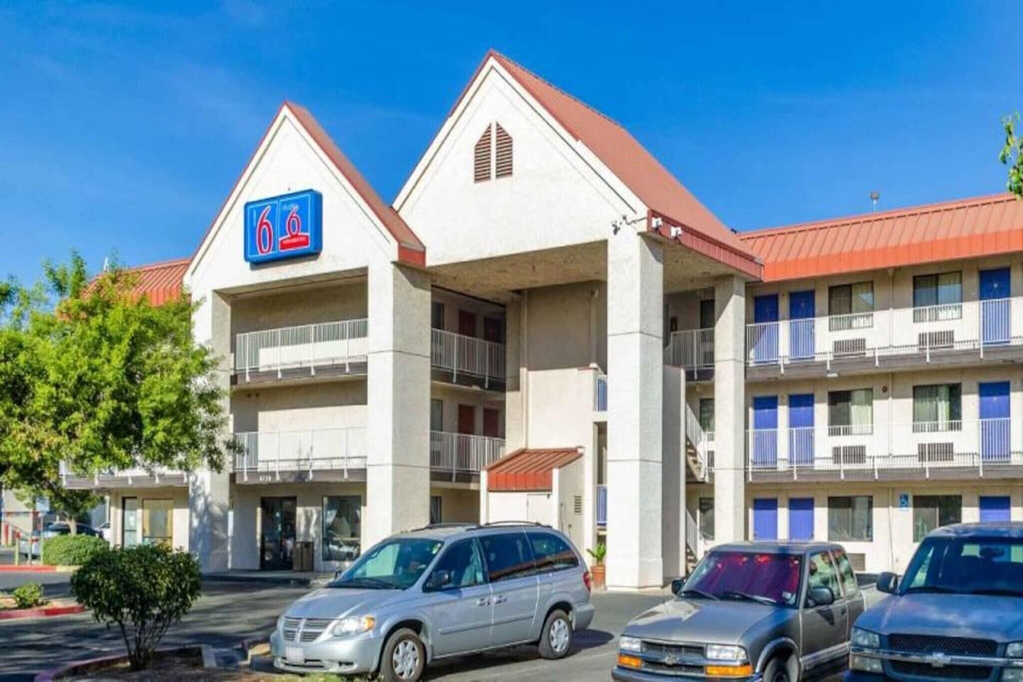 A hotel with a sign indicating 6 rooms, a parking lot, and a red roof.