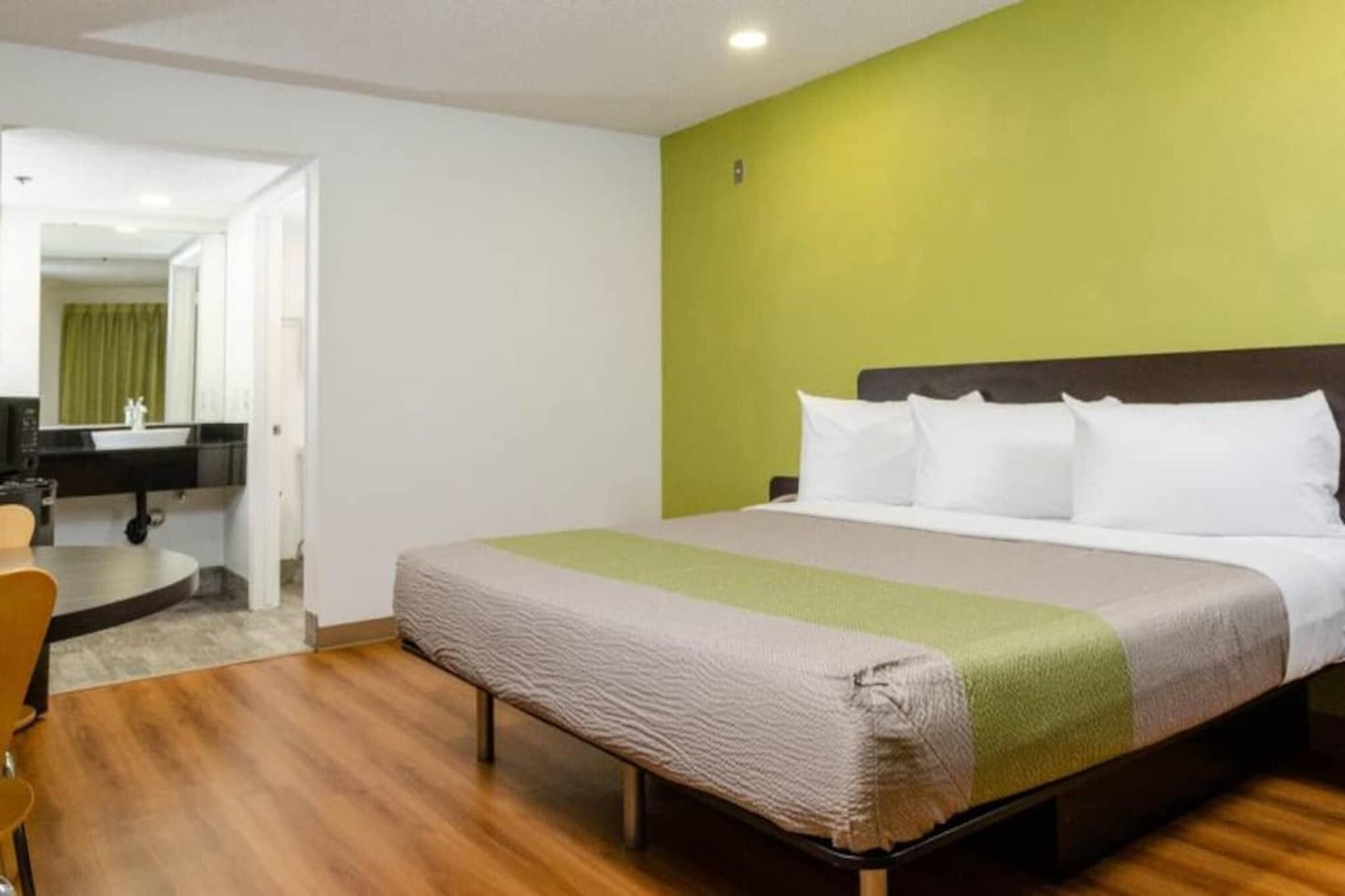 A hotel room with a bed, a desk, a chair, and a mirror.