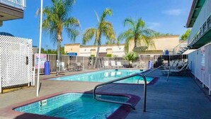 A swimming pool area with lounge chairs, palm trees, and a building in the background. - ADA Queen Bed|RI Shower|Nsmk (Fresno CA)
