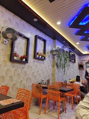A restaurant interior with patterned wallpaper, orange chairs, and ceiling fans. - Vishnu Priya Guest House Ayodhya (Ayodhya)