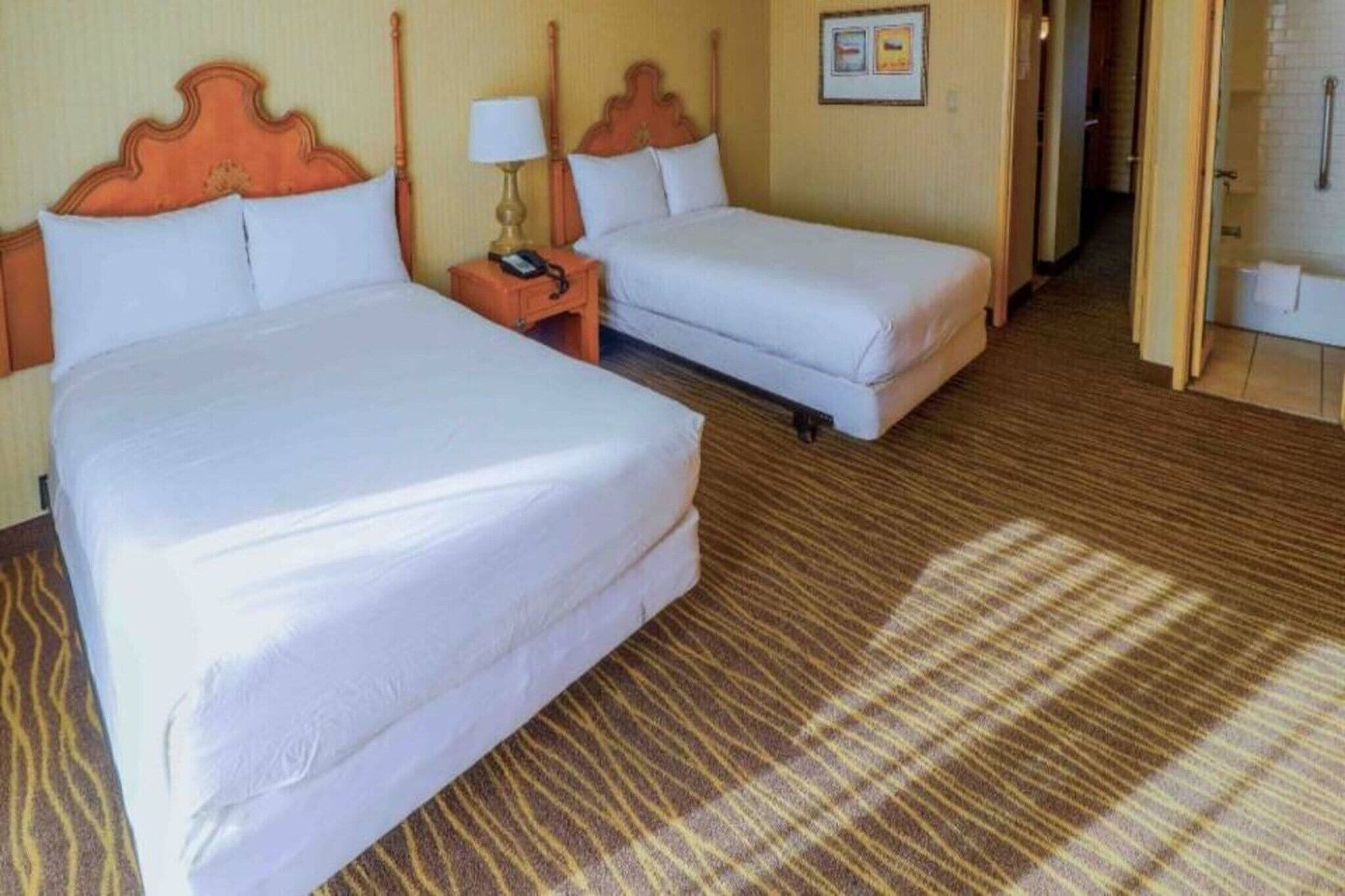 A hotel room with two beds, a nightstand with a lamp, and a shower area.