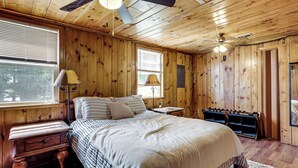 Ein Schlafzimmer mit Holzwänden, einem Bett, Nachttischen, einer Lampe, einem Deckenventilator und einem Fenster.
