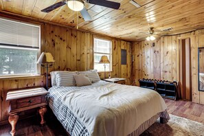 A wooden-paneled bedroom with a bed, nightstands, a lamp, a ceiling fan, and a window. - Boat, Fish, Relax! Crescent Lake Retreat w/ Dock (Rhinelander)