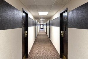 A long hallway with doors on both sides, carpeted floor, and fluorescent lighting.