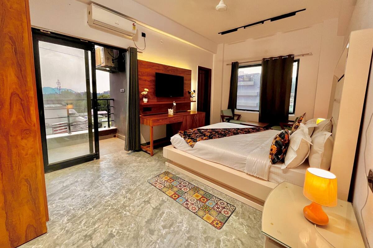 Habitación de hotel con cama, escritorio, televisor, balcón y ventana.