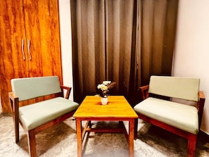 A room with two chairs, a small table, and a curtain. - Hotel Aura Residency Haridwar  (Rishikesh)