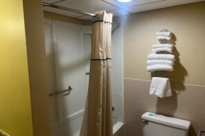 A bathroom with a shower curtain, a toilet, and a stack of towels on a rack.