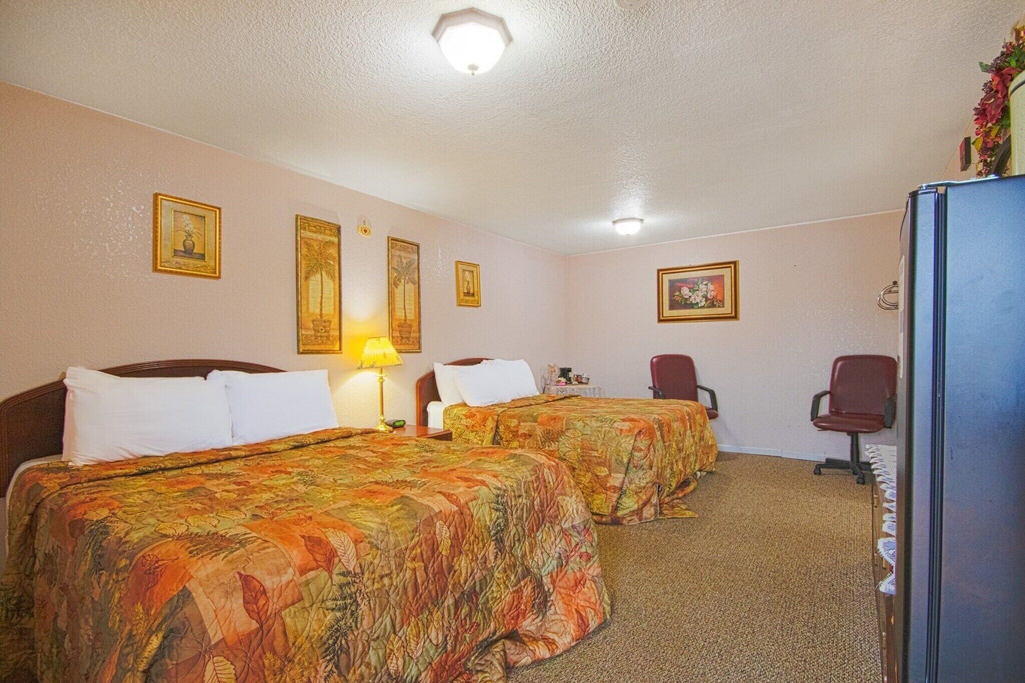A hotel room with two beds, a desk, a chair, and a refrigerator.