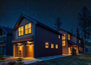 Ein modernes, zweistöckiges Haus mit Garage, großen Fenstern und einer gut beleuchteten Außenansicht bei Nacht.