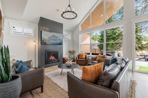 Ein modernes Wohnzimmer mit Kamin, Ledersofas, einem Couchtisch und großen Fenstern mit Blick ins Freie.