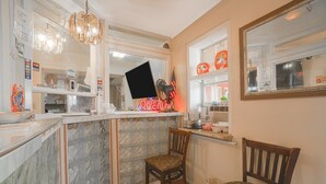 A kitchen with a marble countertop, a wooden chair, a neon sign, and a window with a view of the street.