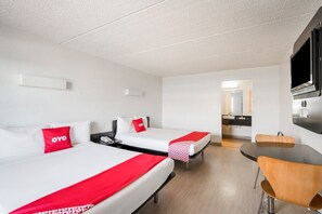 Una habitación de hotel con dos camas, una mesa de comedor, kitchenette y televisión.