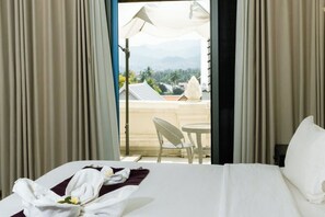 A hotel room with a bed, a chair, and a table with a view of mountains and palm trees.