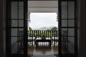 An open doorway leading to a balcony with a table and chairs, overlooking a mountainous landscape.