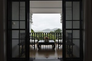 An open doorway leading to a balcony with a table and chairs, overlooking a mountainous landscape.