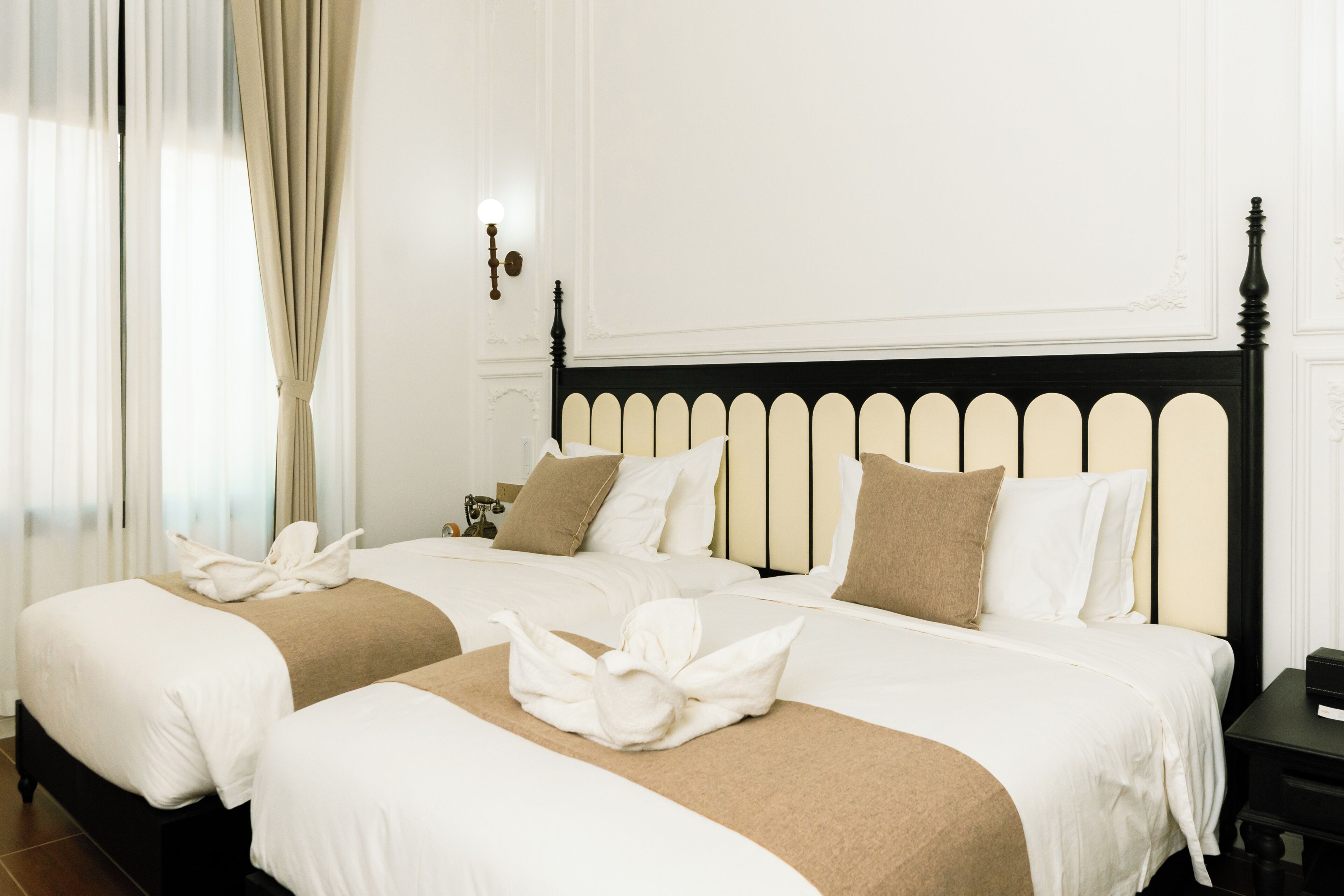 A hotel room with two beds, a black headboard, white bedding, and a nightstand with a lamp.