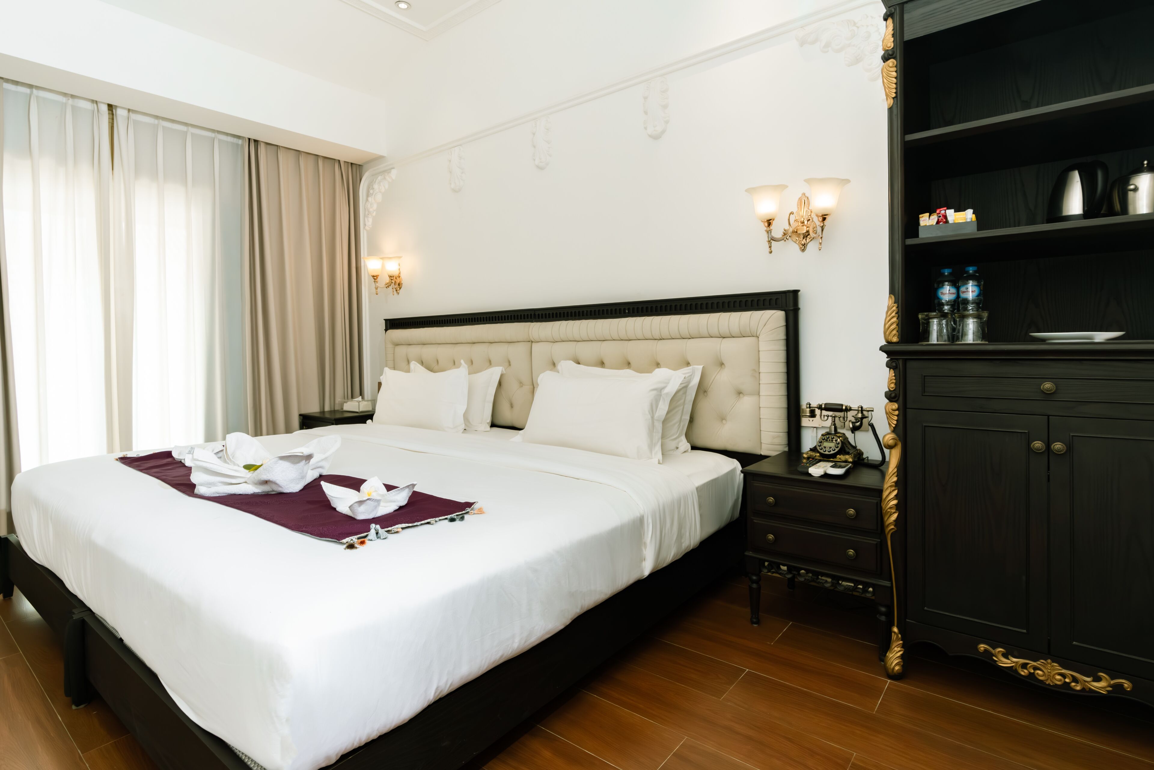A hotel room with a large bed, a nightstand, a wardrobe, and a chandelier.