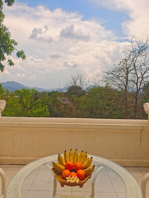 A table with a fruit bowl on a balcony overlooking a mountainous landscape. - Jing Land Palace Hotel Luang Prabang (Luang Prabang)