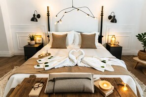 A neatly arranged hotel room with a large bed, bedside tables with lamps, a bedside plant, and a wooden side table with a candle and books. - Jing Land Palace Hotel Luang Prabang (Luang Prabang)