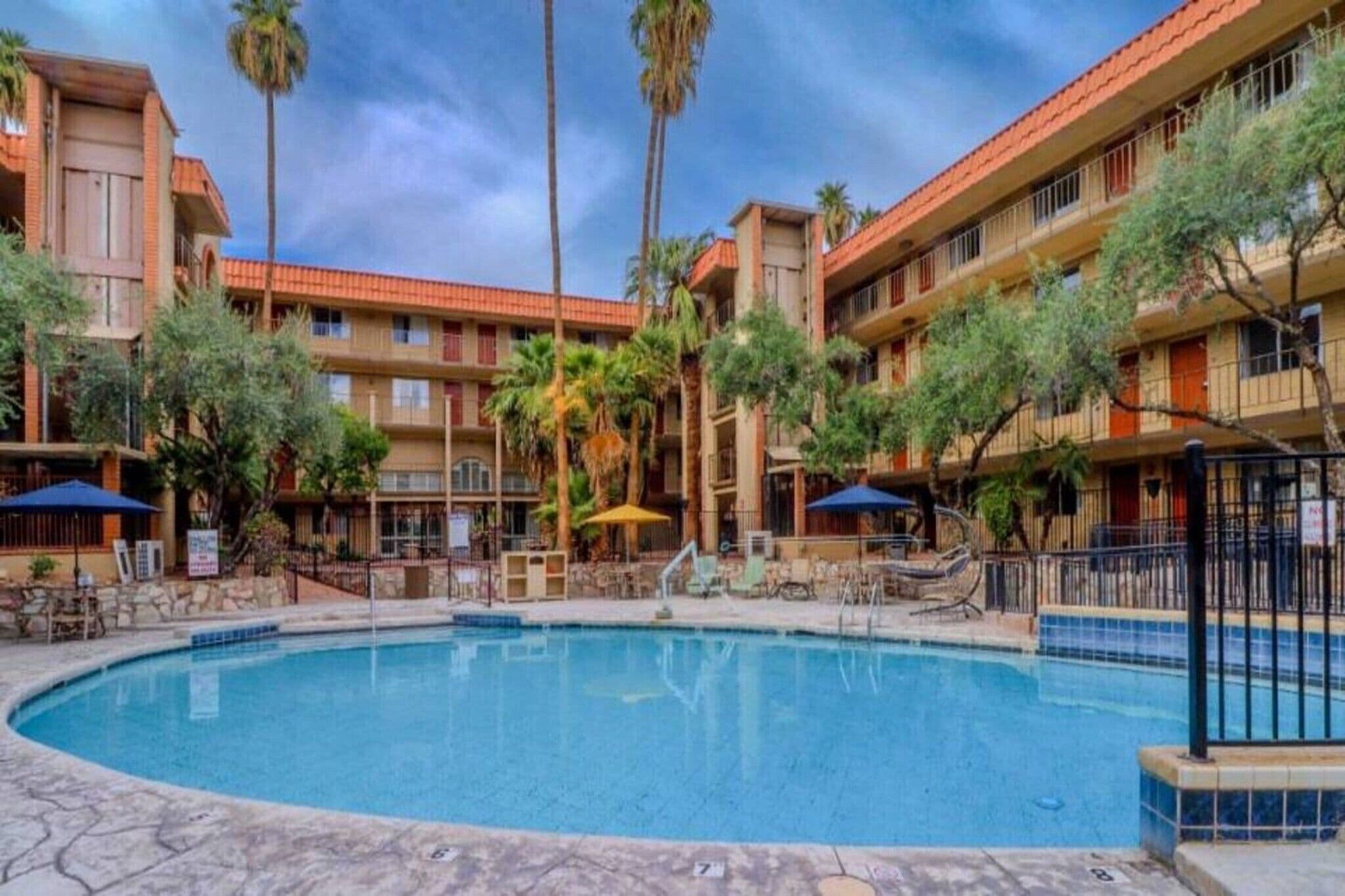 A hotel with a swimming pool, palm trees, and outdoor seating areas.