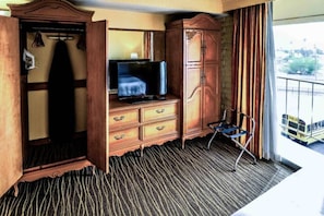 Habitación de hotel con televisión, armario y una silla cerca de una ventana que da a un autobús.