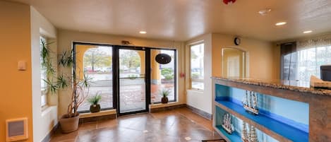 A hotel lobby with a reception desk, potted plants, and a view through the glass doors.