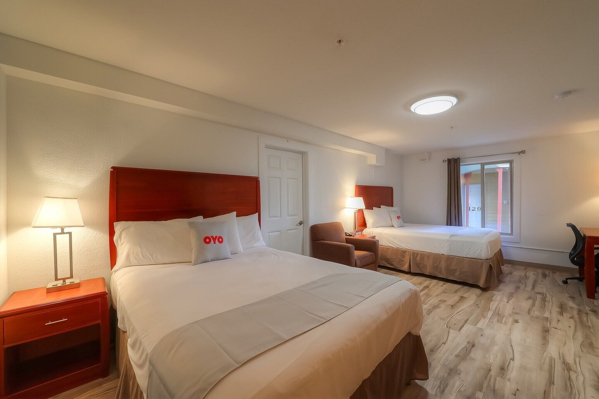 Une chambre d’hôtel avec deux lits, une table de chevet, une chaise, un bureau et une fenêtre avec des rideaux.