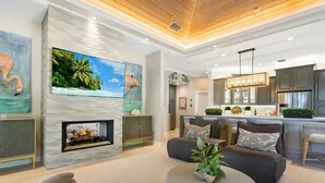 A modern living room with a fireplace, a television, and a kitchen area with dark cabinets. - Casey Key Paradise~Private Beach~Gulf to Bay (Nokomis)