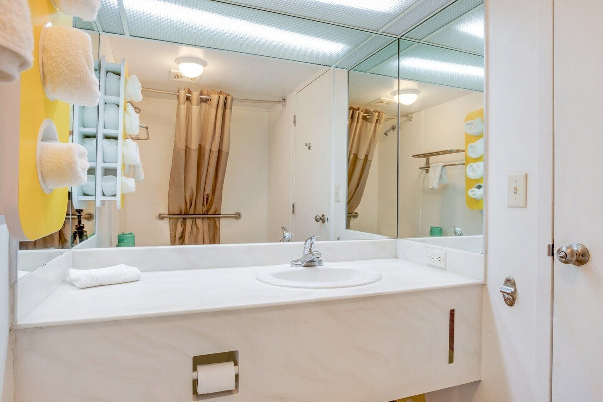 Un baño con un espejo grande, lavamanos blanco y barra para toallas.