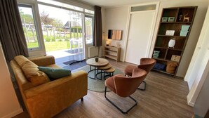 Una sala de estar con un sofá, dos sillones, una mesa de centro, un televisor y una estantería.
