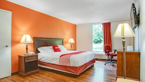A hotel room with a bed, two bedside lamps, a desk, a chair, and a window with curtains.