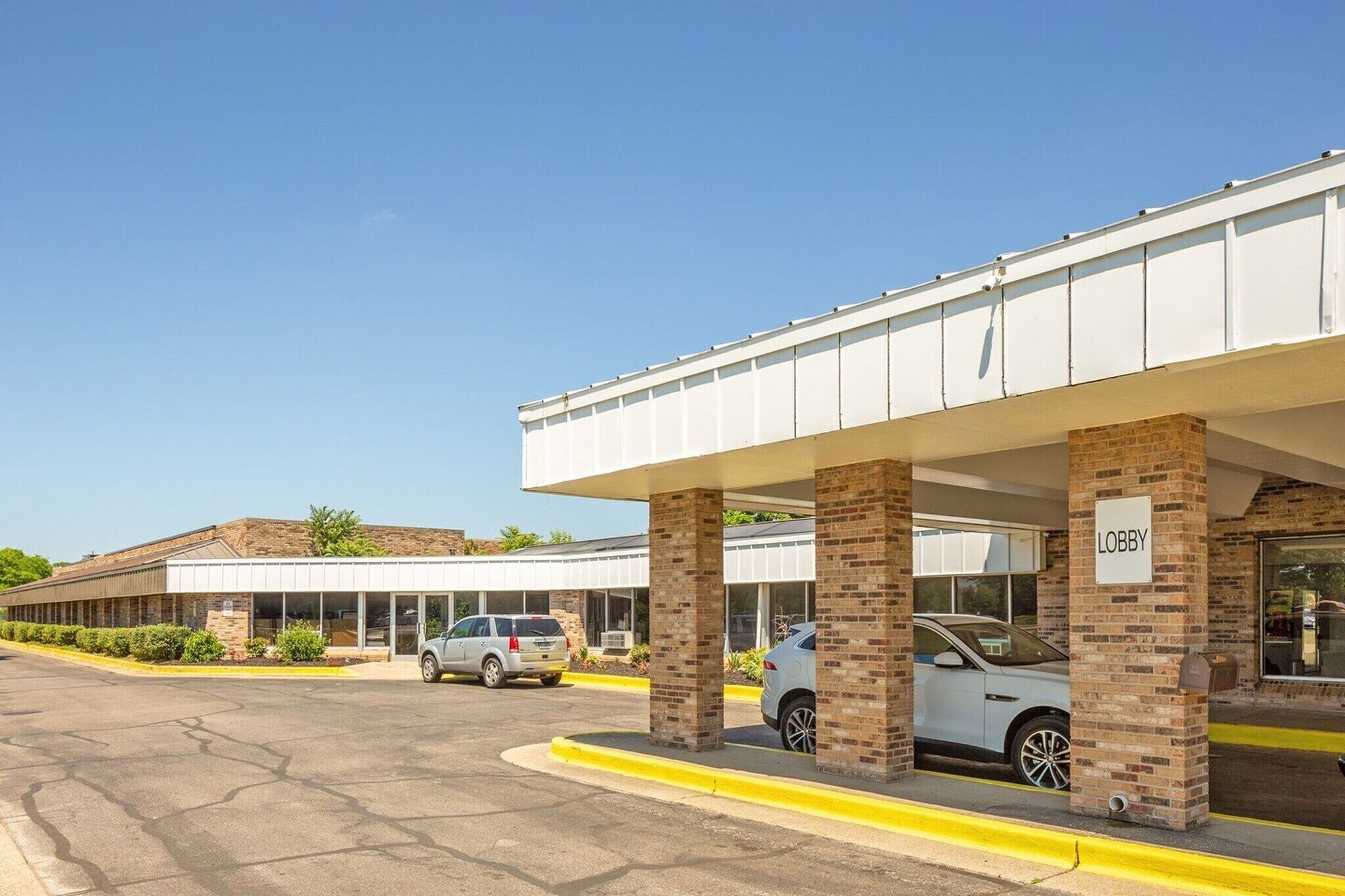 Un bâtiment doté d’un hall d’entrée abrité, d’un parking et offrant une vue sur un ciel dégagé.