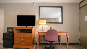 Une chambre d’hôtel équipée d’un bureau en bois, d’une télévision, d’une lampe, d’une chaise, d’un four à micro-ondes et d’un réfrigérateur.