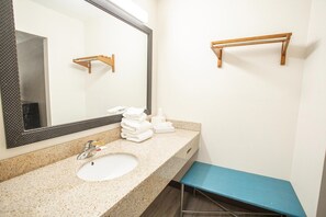 A bathroom with a sink, mirror, towel rack, and a blue bench.
