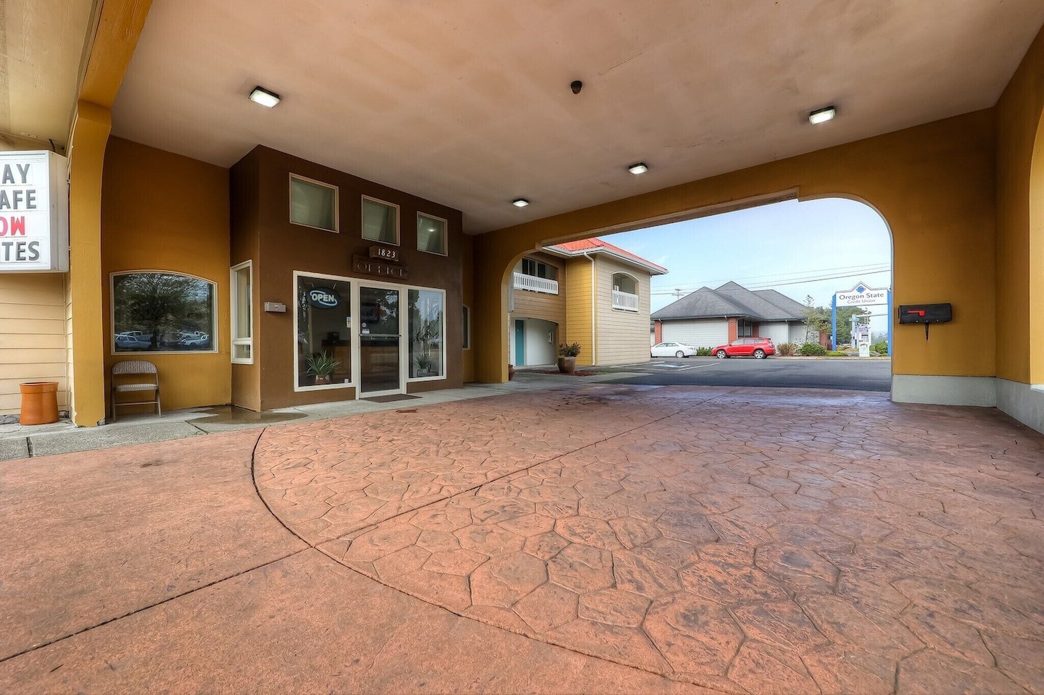 A hotel entrance with a covered walkway, a sign indicating 'Open,' and a visible address number.