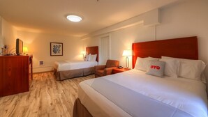 A hotel room with two beds, a desk, a chair, and a lamp.