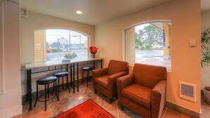 A modern kitchen with a bar area, two armchairs, and a large window with a view of the street.