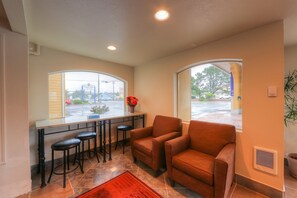 A modern kitchen with a bar area, two armchairs, and a large window with a view of the street.