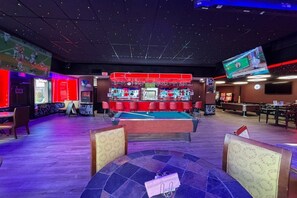 A billiards room with a pool table, red seating, and a television screen.