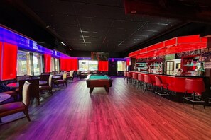 A billiards room with a pool table, red bar area, and seating.