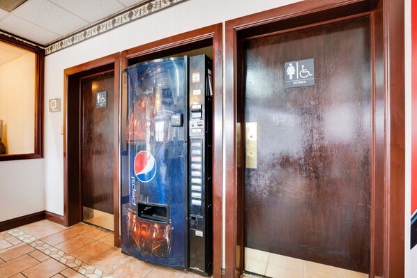 A hallway with a vending machine, a door with a wheelchair accessibility sign, and another door with a women-only sign.