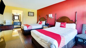 Une chambre d’hôtel avec deux lits, un coin salon, un miroir, une télévision et une salle de bain visible à travers une porte ouverte.