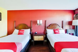 A hotel room with two beds, a nightstand, a lamp, and a wall-mounted light fixture.