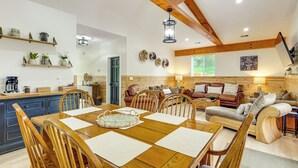 A spacious living area with a wooden dining table, chairs, a sofa, and a coffee table. There are shelves with decorative items and a clock on the wall. - 3 Mi to Lake! Golfer's Oasis on Summit Course (Bellaire)