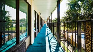 A covered corridor with a blue pathway, large windows, and a view of a pool and palm trees.