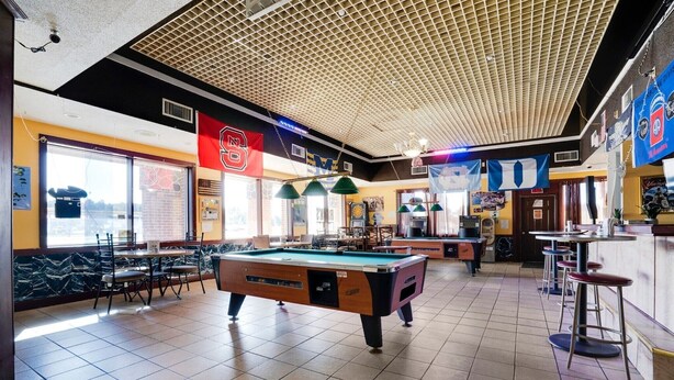 A pool table in a room with a high ceiling and a bar area.