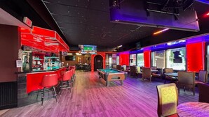 A billiards room with a pool table, red bar area, and seating.