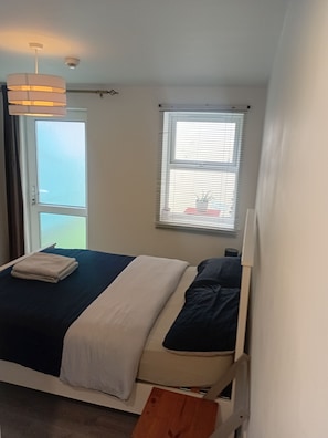 Ein Schlafzimmer mit Bett, Fenster mit Jalousien, Deckenleuchte und Tür.