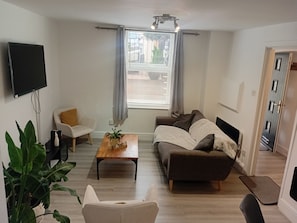 Ein Wohnzimmer mit Sofa, Couchtisch, Fernseher und einem Fenster mit Vorhängen.