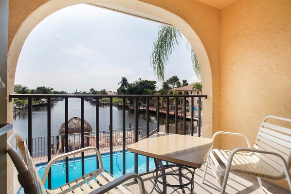 A balcony with a pool, chairs, and a view of a water body and buildings.